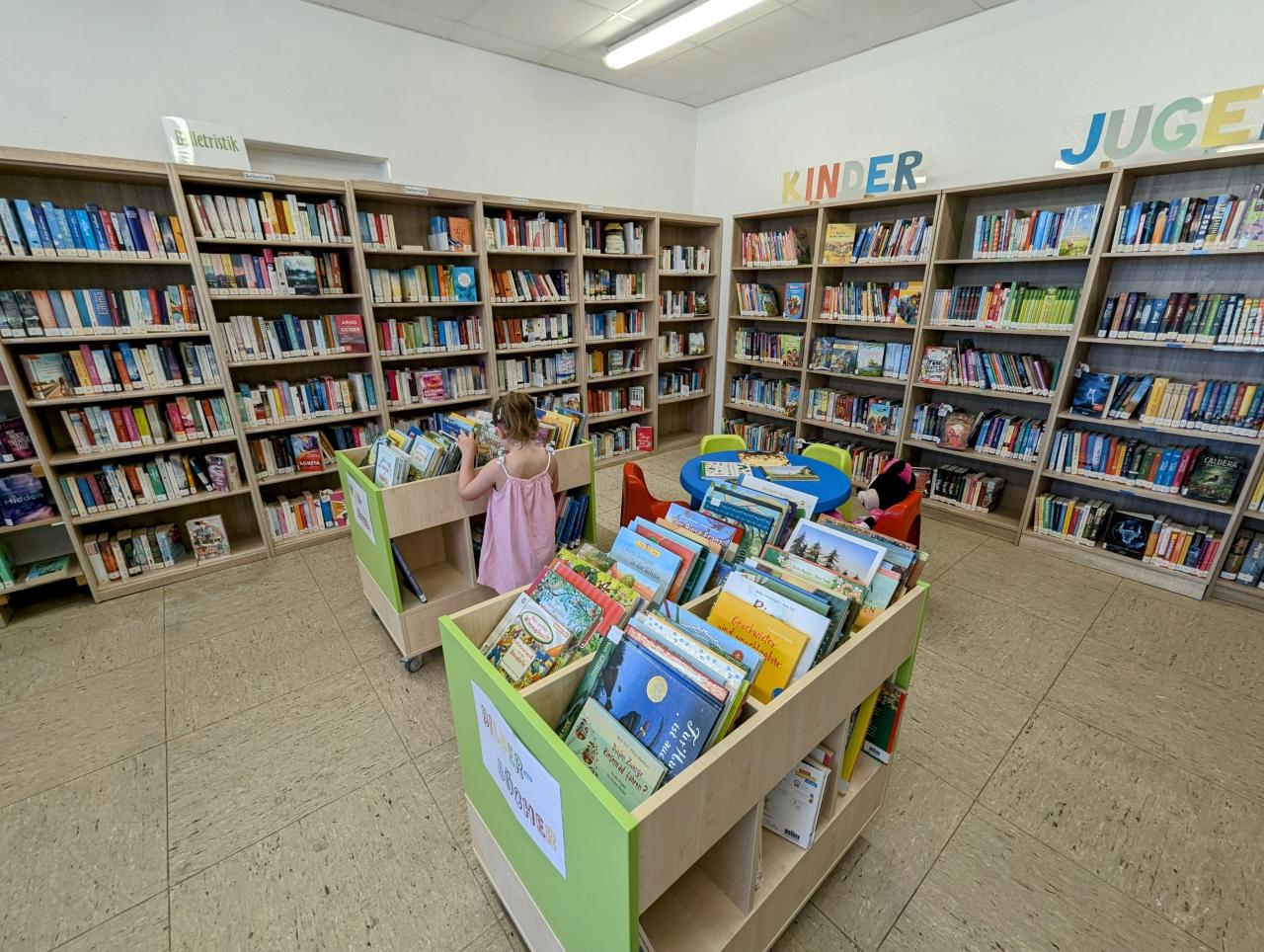 Mädchen vor Buchregal und Bücherwägen