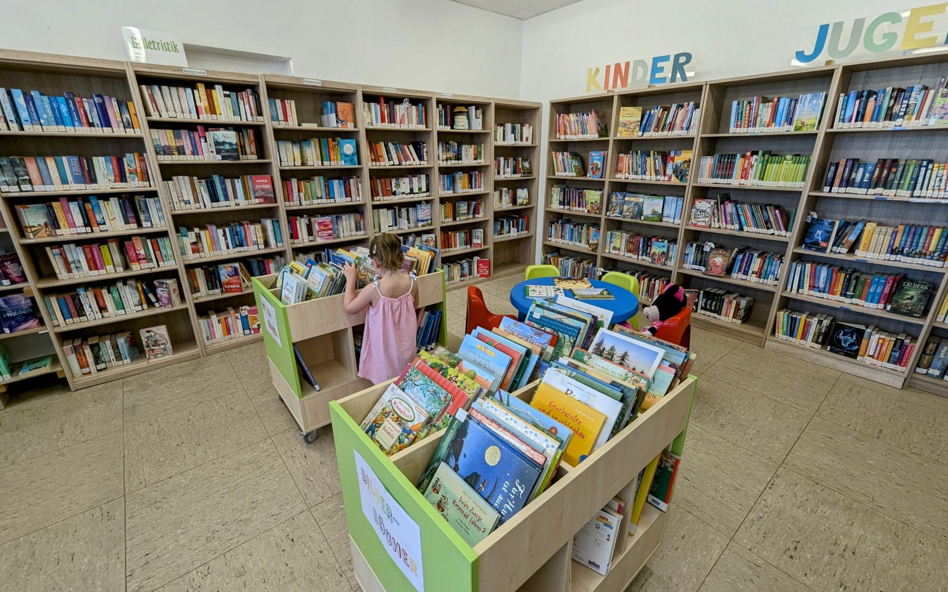 Mädchen vor Buchregal und Bücherwägen